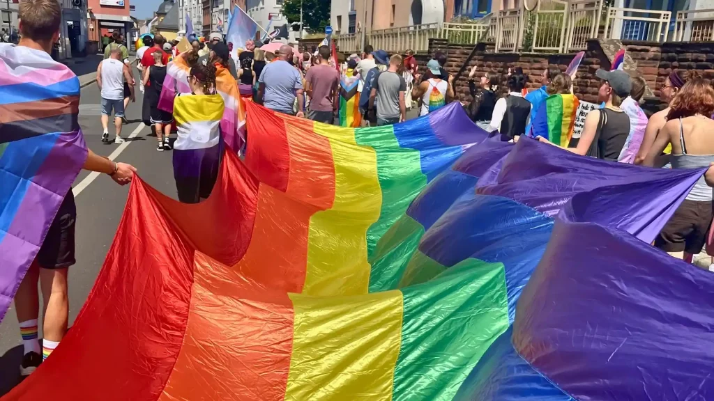 Teilnehmende der CSD-Parade tragen gemeinsam eine große Regenbogenflagge durch die Innenstadt.