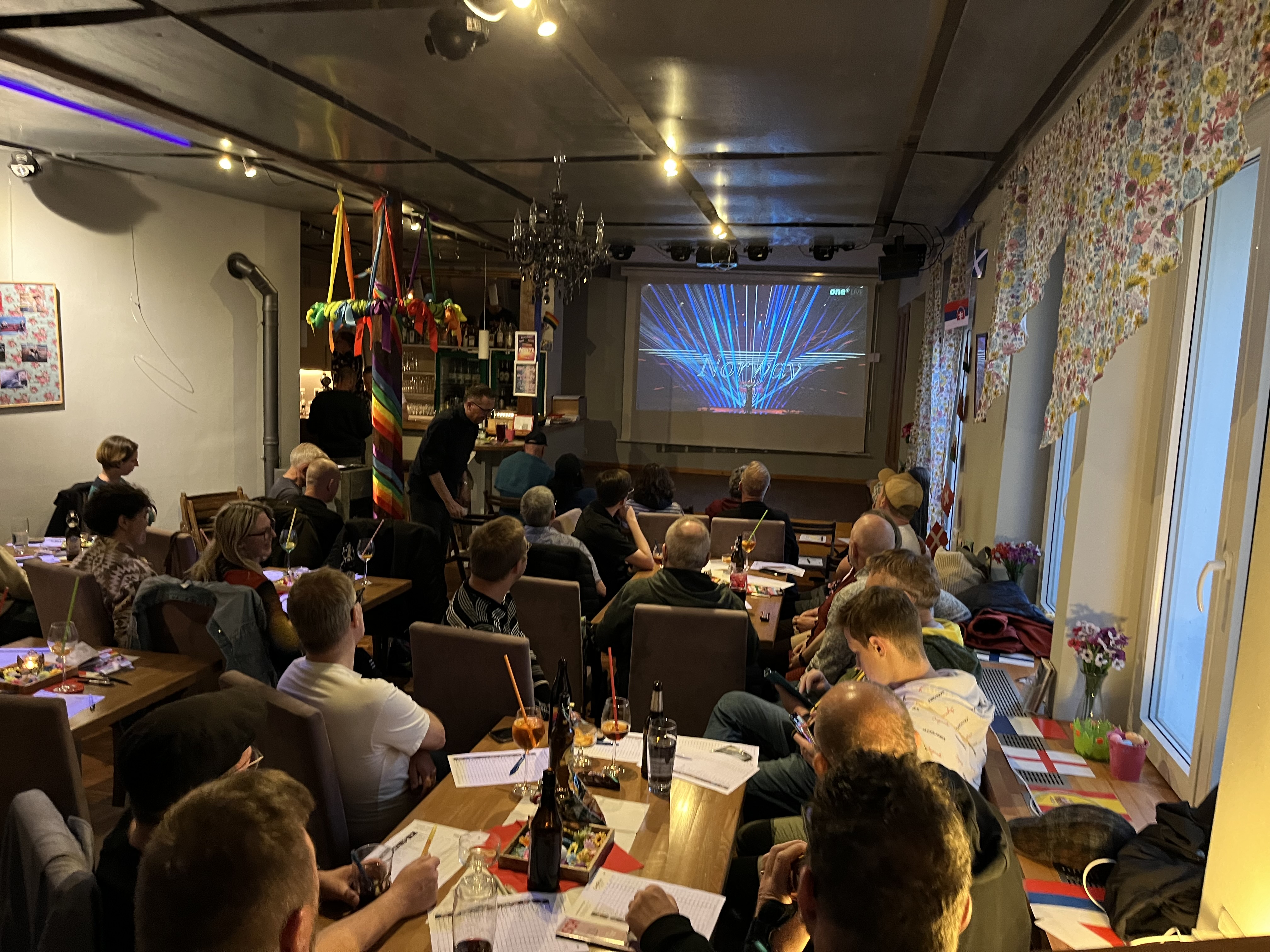 Menschen halten eine große Regenbogenflagge auf dem Marktplatz in Würzburg während einer queeren Aktion des WuF-Zentrums.